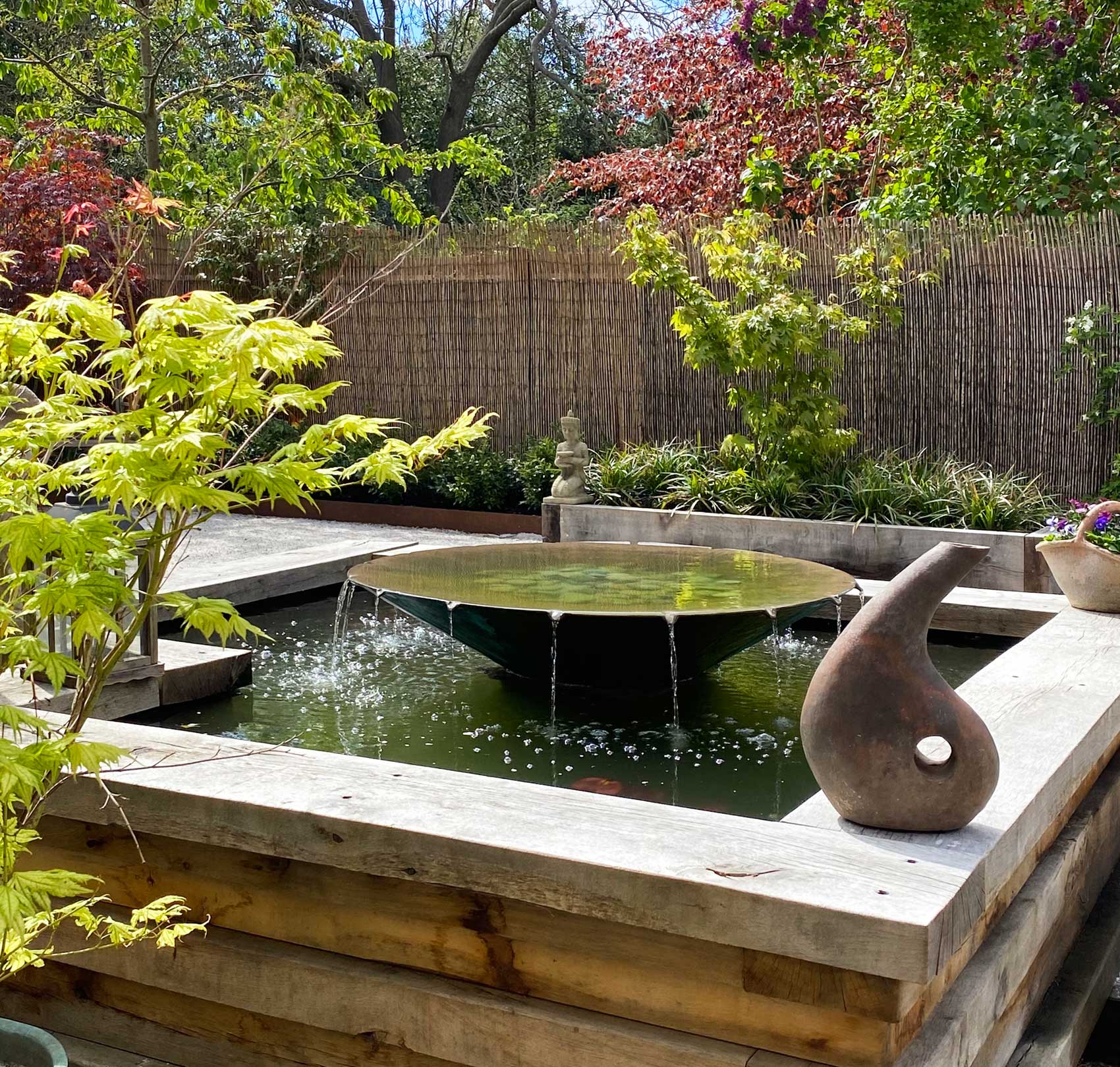 Raised pond with layered oak walls and Trasimeno saucer water feature designed by Peter Eustance